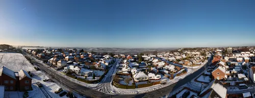 This image presents a wide panorama of Bolsover on a winter morning, with the town's urban landscape blanketed in fresh snow. The houses and streets are clearly visible, with rooftops and roads covered in a layer of white, highlighting the wintry atmosphere. Fields stretch out on the left side of the image, also dusted with snow, contrasting with the more densely built areas and contributing to the scene's seasonal charm. The clear blue sky above adds to the bright, crisp feel typical of winter mornings. The photograph captures the essence of Bolsover's urban area, showing the mix of residential neighborhoods and open fields, and is classified as an urban landscape image.